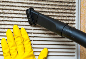 Hand in yellow glove and vacuum cleaner pipe. Ventilation grill cleaning